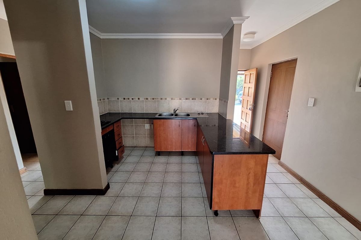 A functional kitchen featuring l-shaped cabinetry, granite countertops, a double bowl sink, and neutral ceramic tile flooring.