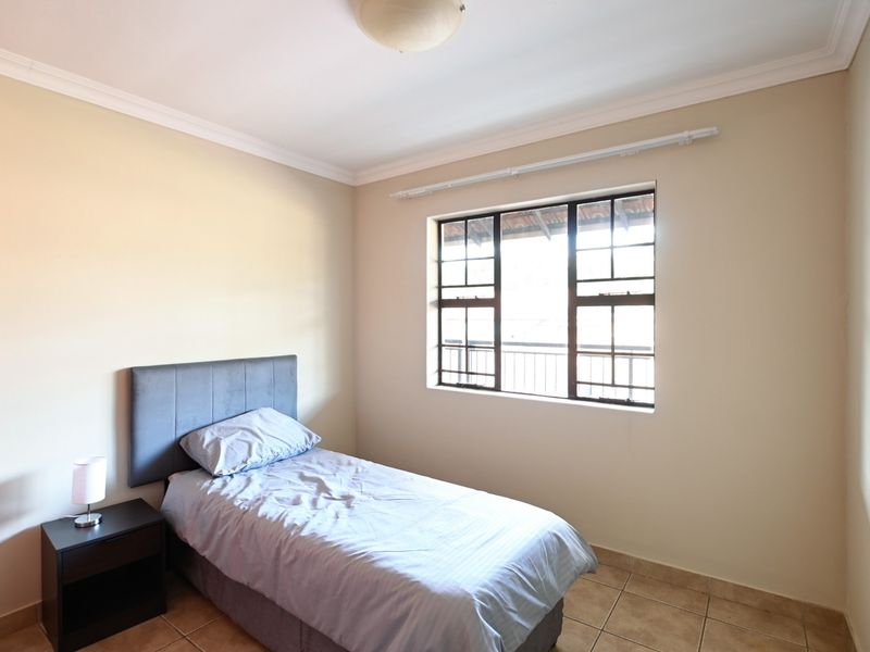 A functional bedroom featuring tiled flooring, coved ceilings, and a window fitted with security bars and a curtain rail.