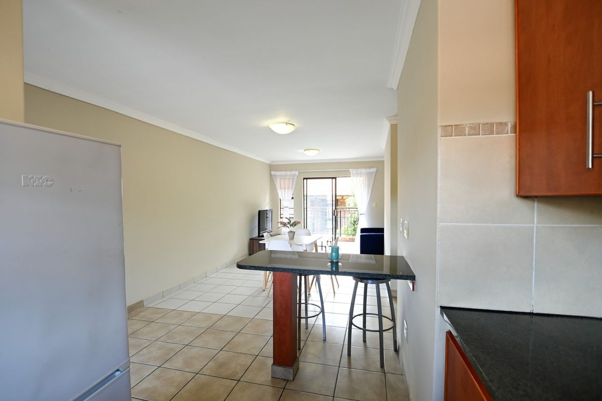 Open-plan living and kitchen area featuring tiled flooring, a granite breakfast bar, and a sliding door leading to an outdoor balcony.