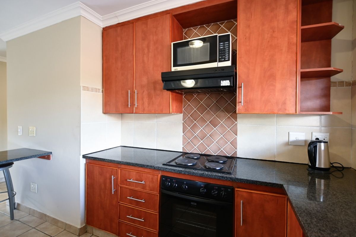 A functional kitchen featuring warm-toned wooden cabinetry, granite countertops, a built-in oven, electric hob, and a convenient breakfast bar area.