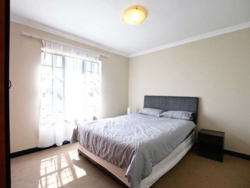 A functional bedroom featuring carpeted flooring, built-in cupboards, and security bars on the window, providing a neutral space ready for personalization.