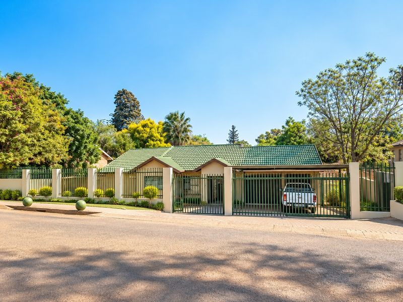 Front view of a well-maintained single-story house featuring a green tiled roof, secure perimeter fencing, and a gated carport entrance.
