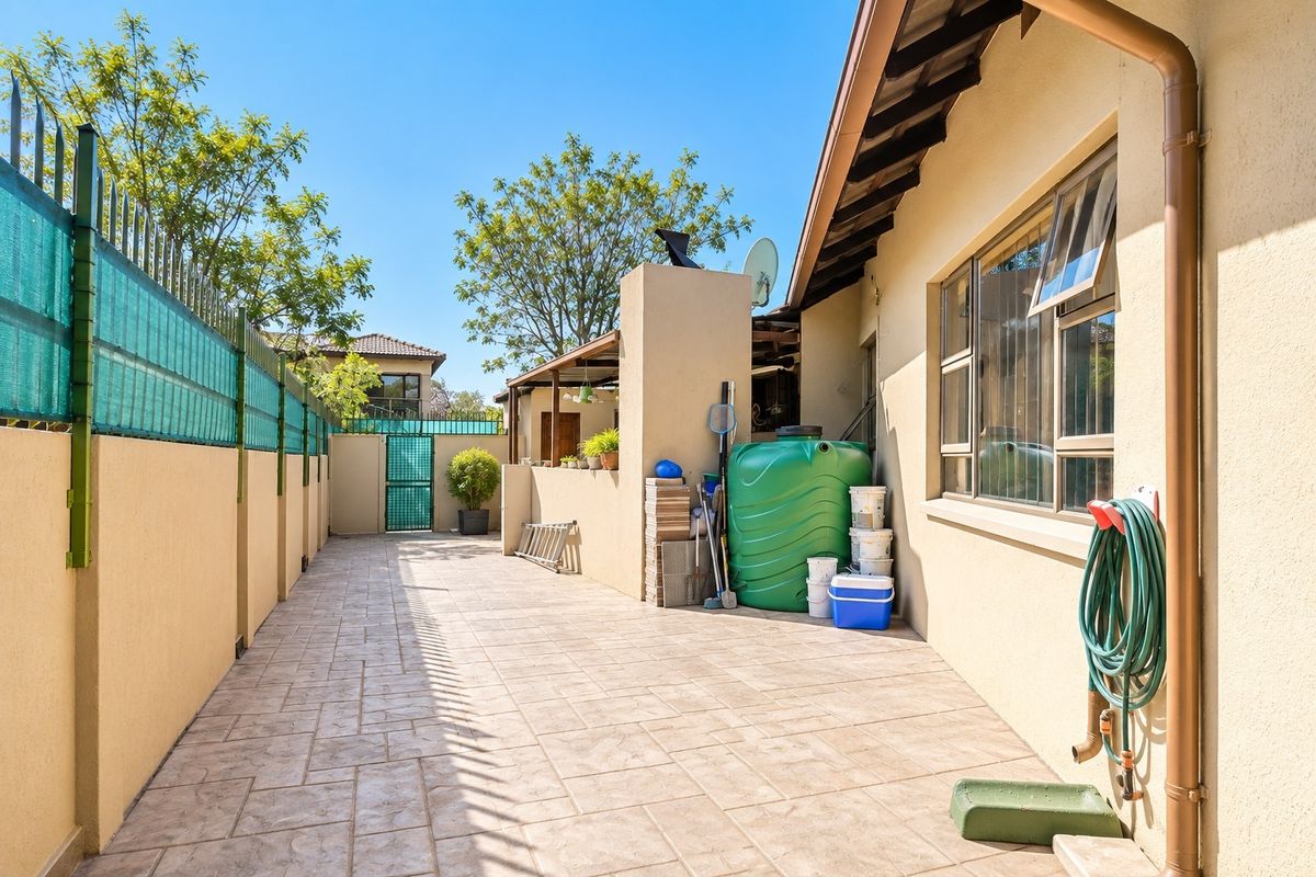 A paved rear courtyard area featuring a boundary wall with security fencing, a water storage tank, and external plumbing fixtures.