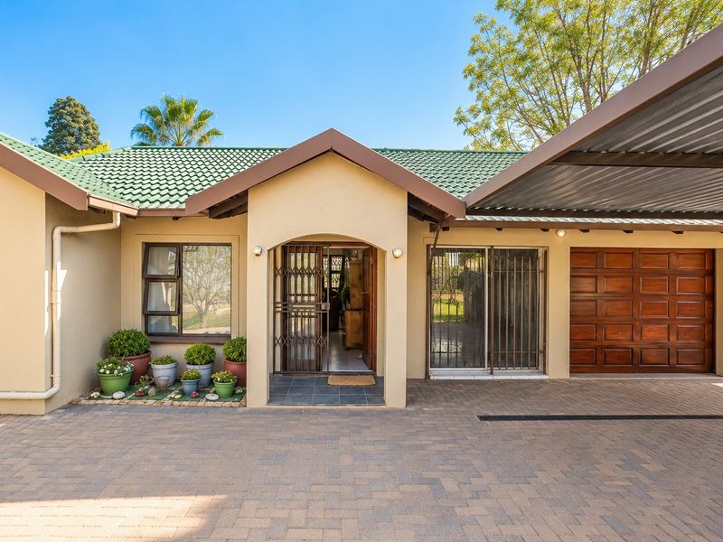 Front elevation of a well-maintained house featuring a paved driveway, covered carport, wooden garage door, and secure entrance with tiled roof.