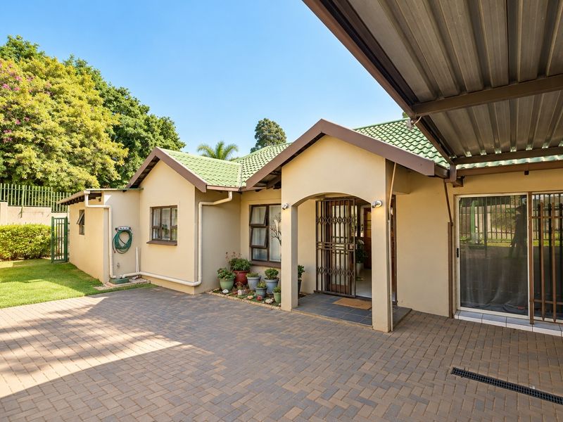 Front exterior view of the house featuring a paved driveway, covered carport, and a well-maintained entrance with security gate.