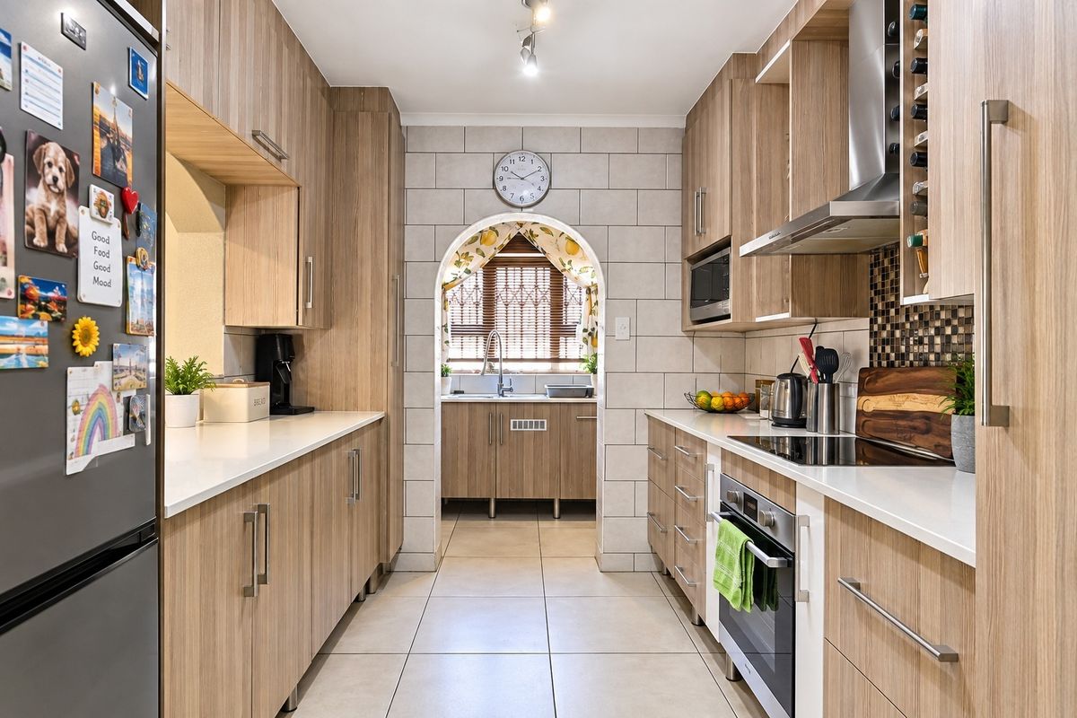 Modern galley-style kitchen featuring wood-grain cabinetry, stone countertops, integrated appliances, and a separate scullery area accessed through a charming arched doorway.