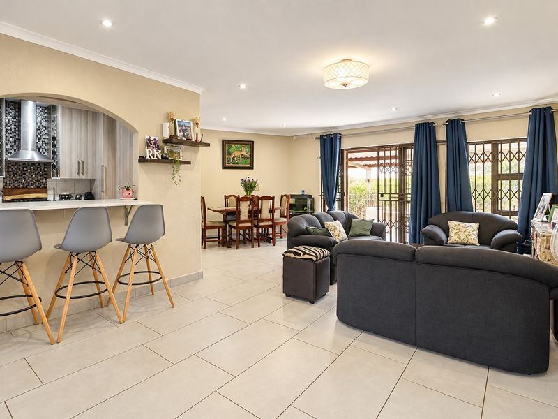 Spacious open-plan living area featuring a modern kitchen with breakfast bar, tiled floors, and direct access to the outdoor patio through security gates.