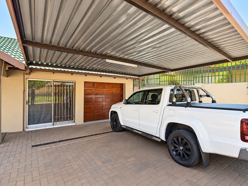 A well-maintained paved driveway featuring a covered carport, a sectional garage door, and a secure sliding glass entrance.