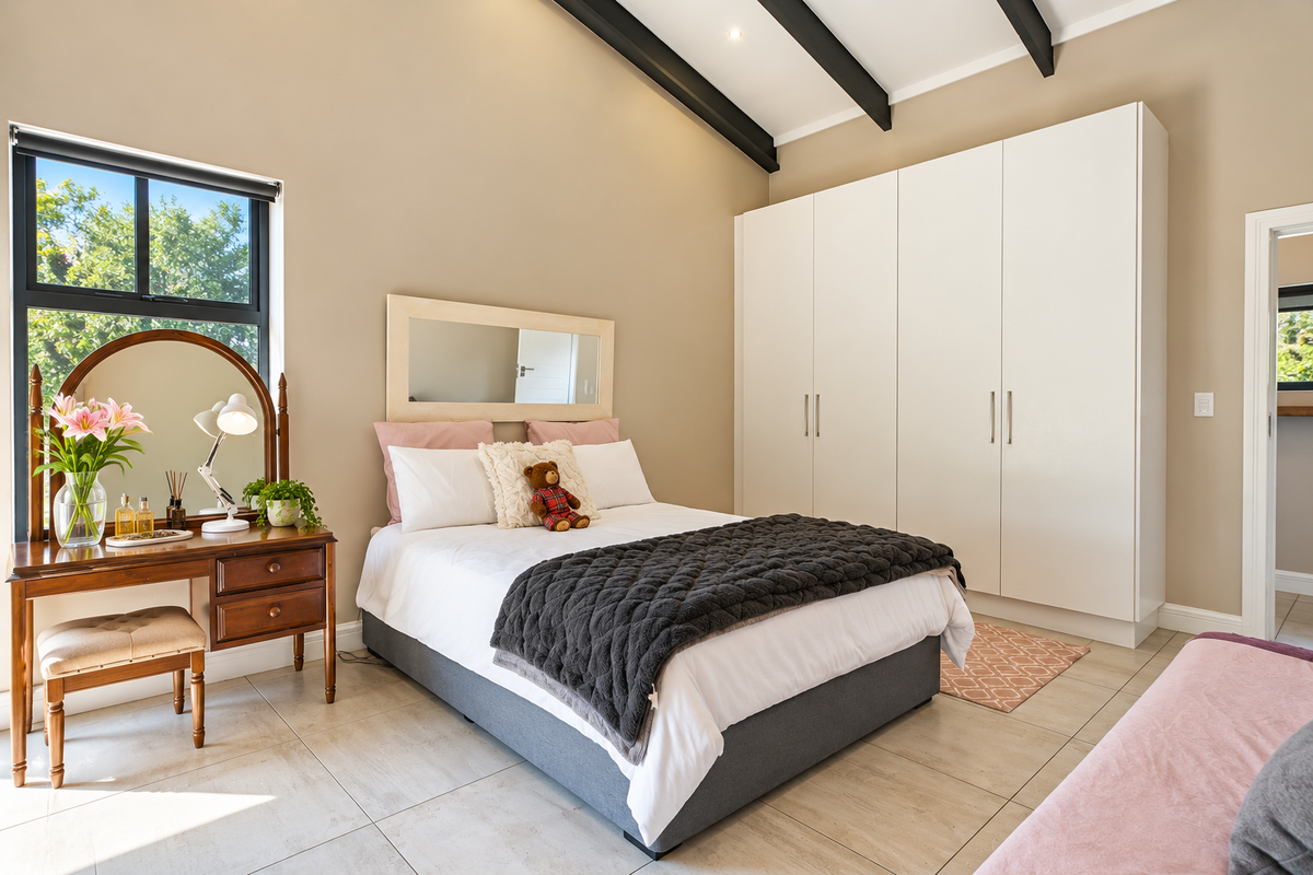 A well-maintained bedroom featuring exposed ceiling beams, neutral tiled flooring, and ample built-in wardrobe storage with a large window providing natural light.