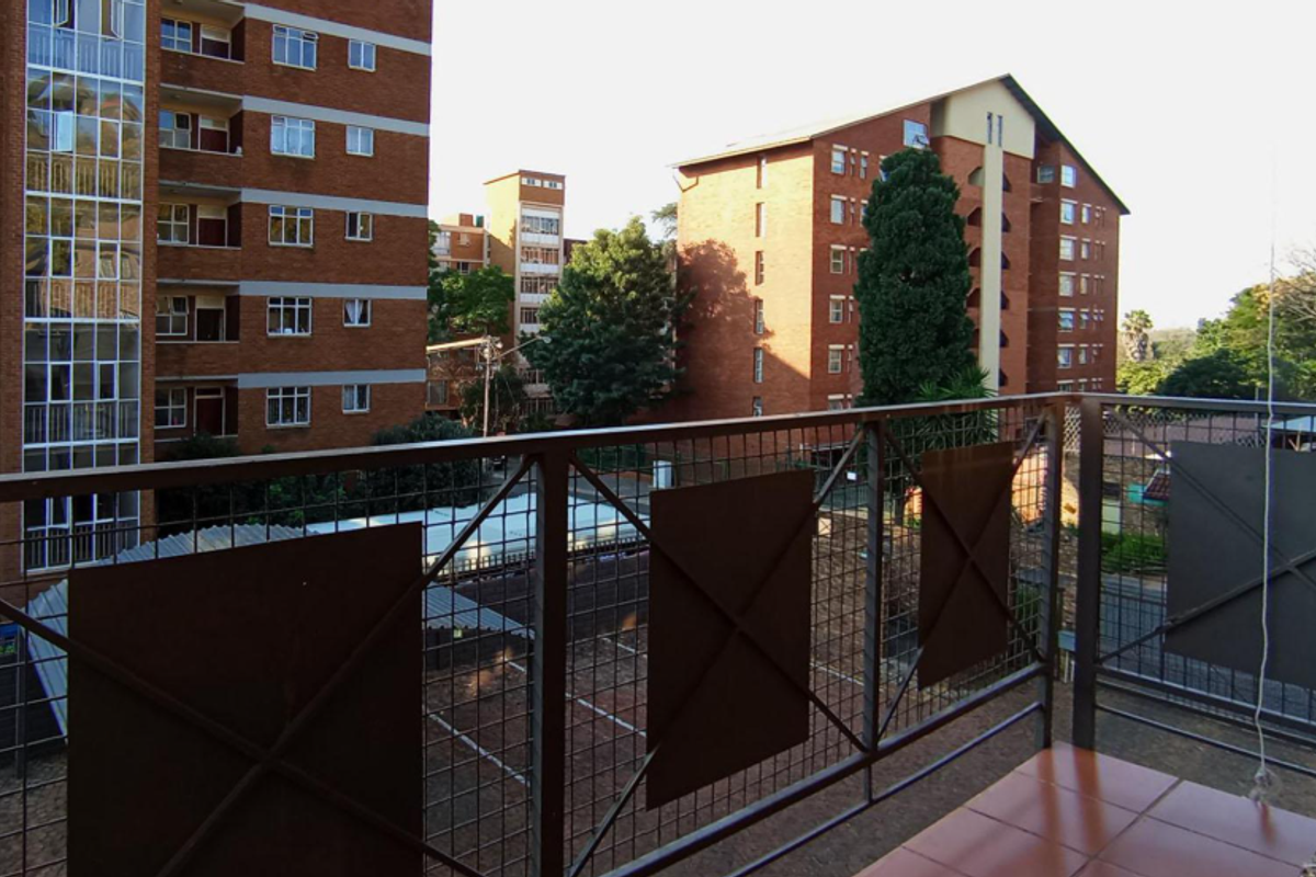 A balcony featuring a metal balustrade and tiled flooring, overlooking the surrounding residential complex and parking area.