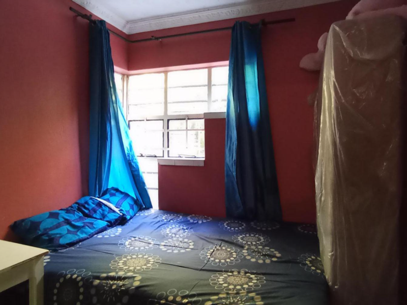 A bedroom featuring red walls, a metal-framed window, and decorative ceiling cornice, offering a functional space ready for modernization.