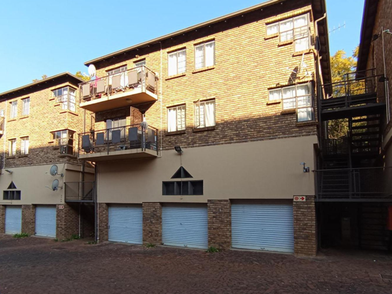 Exterior view of a multi-story townhouse complex featuring brick facade, multiple balconies, and ground-level metal roller garage doors.