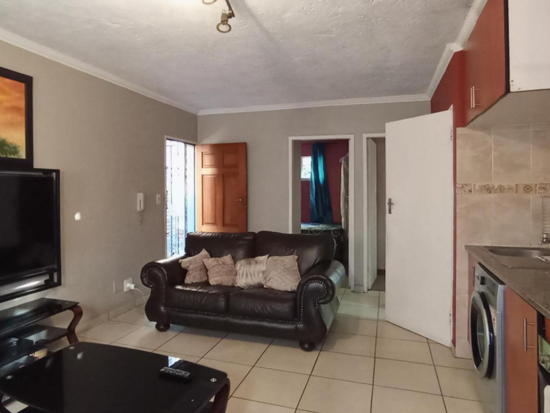 Open-plan living area featuring tiled flooring, coved ceilings, and a compact kitchen with built-in cabinetry and integrated cooking appliances.
