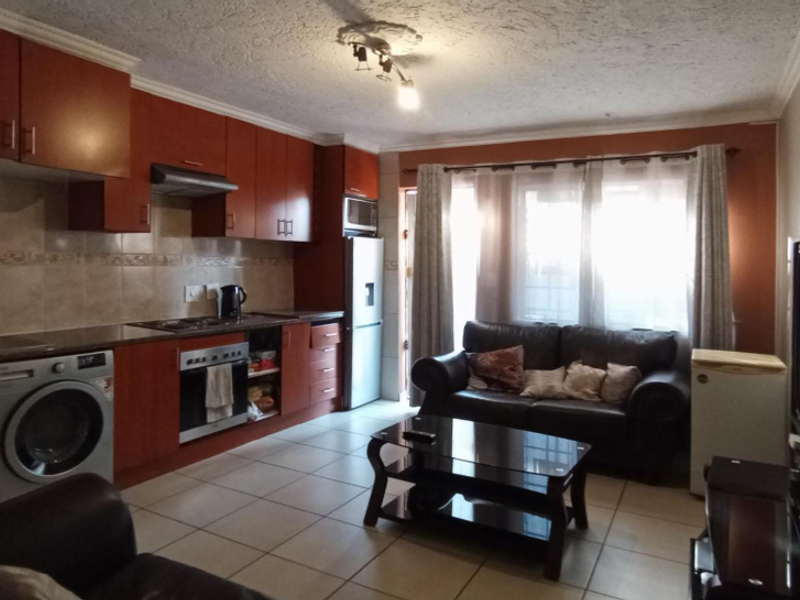 Open-plan living area featuring a functional kitchen with built-in cabinetry, oven, hob, and tiled flooring throughout the combined space.