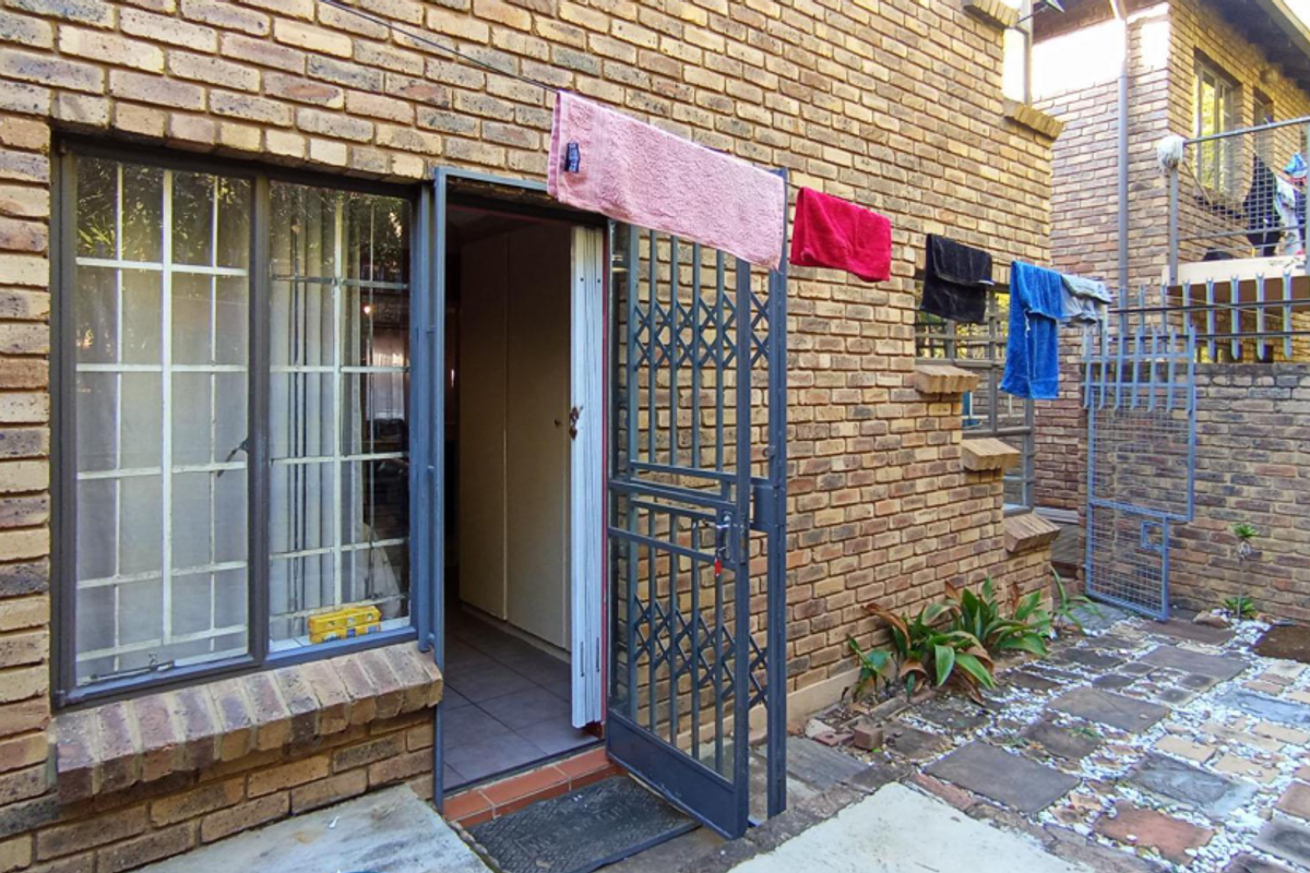 Rear exterior view of a face brick townhouse featuring a paved courtyard, security gate, and steel window frames.