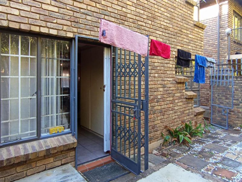 Rear exterior view of a face brick townhouse featuring a paved courtyard, security gate, and steel window frames.
