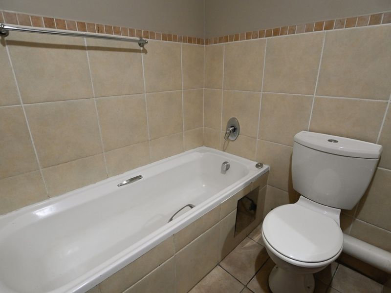 A functional bathroom featuring a built-in bathtub, toilet, and neutral wall tiling. The space is clean but requires minor maintenance to the bathtub panel.