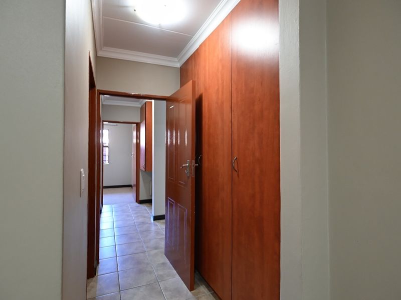 A functional hallway featuring tiled flooring and extensive built-in wooden cupboards, providing ample storage space and connecting to adjacent rooms.