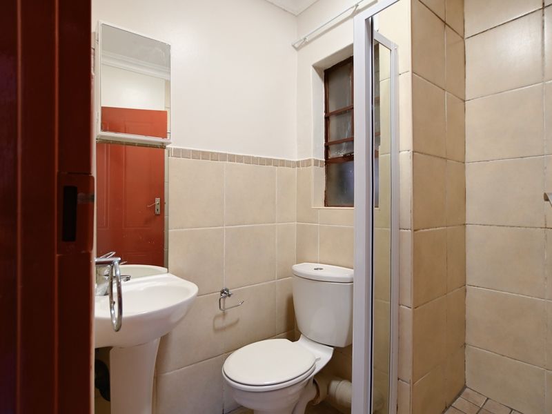 A compact bathroom featuring a pedestal basin, toilet, and shower enclosure with neutral wall tiling.
