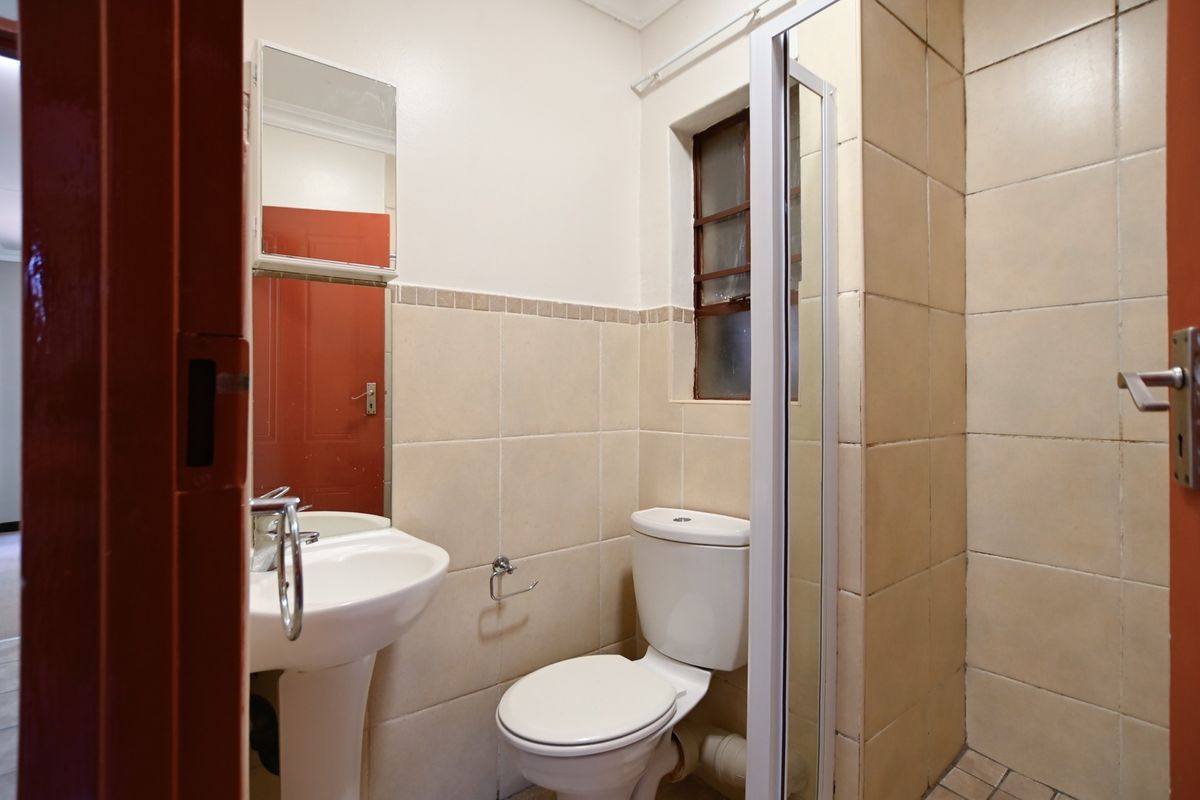 A compact bathroom featuring a pedestal basin, toilet, and shower enclosure with neutral wall tiling.