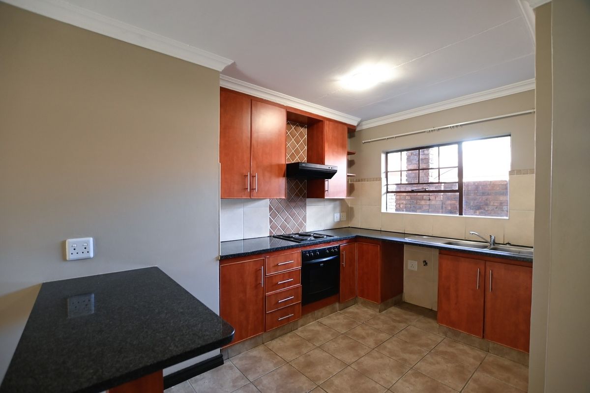 A functional kitchen featuring cherry-wood cabinetry, granite countertops, built-in oven with hob, extractor fan, and a breakfast nook area.