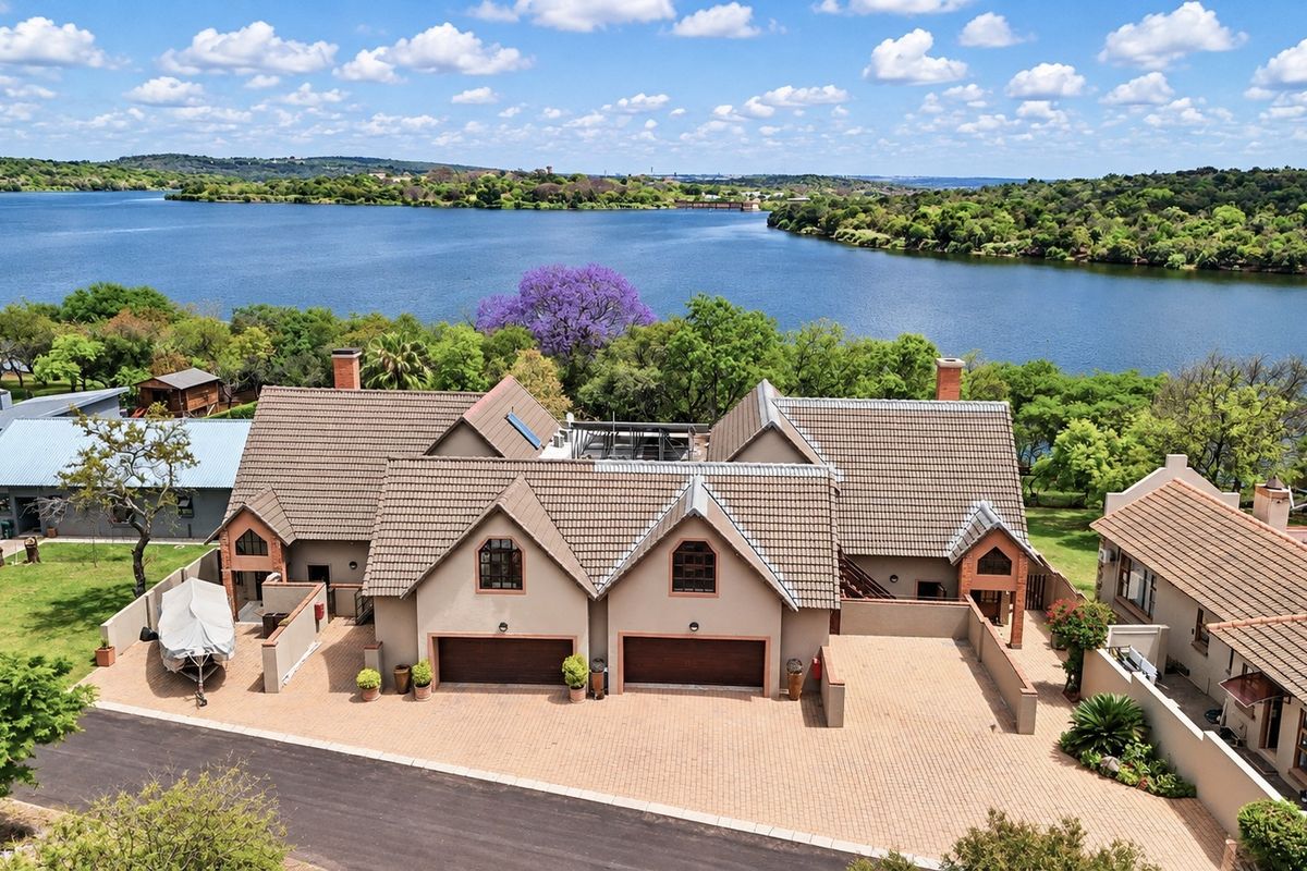 Aerial view of a residential property featuring a double garage, tiled roof, and paved driveway, situated in a scenic waterfront location.