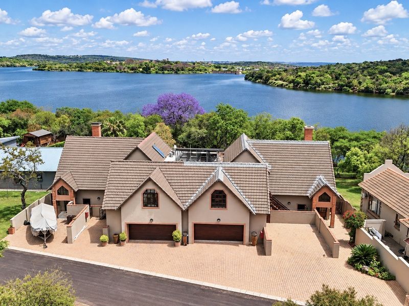 Aerial view of a residential property featuring a double garage, tiled roof, and paved driveway, situated in a scenic waterfront location.