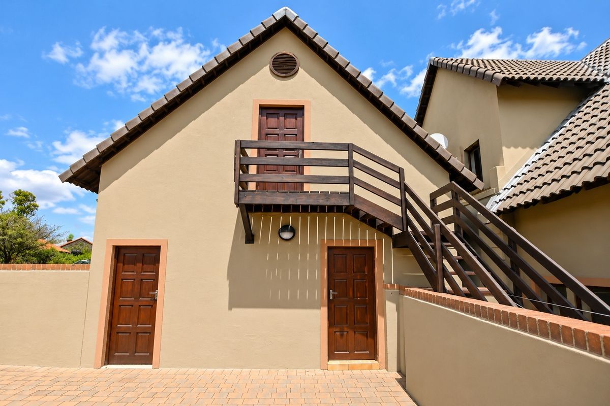 Rear exterior view of the property featuring a paved courtyard, timber staircase leading to an upper balcony, and traditional tiled roofing.