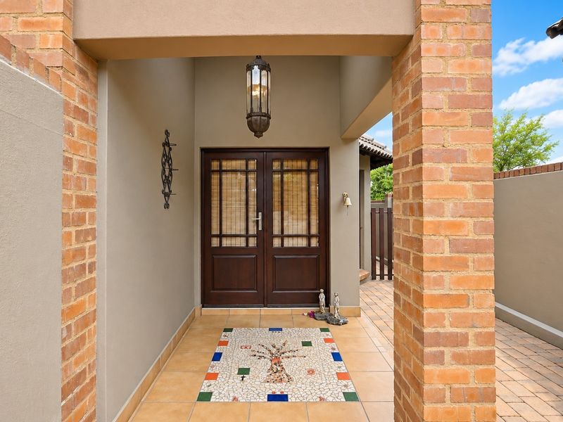 A welcoming covered entrance featuring brick pillars, a decorative mosaic floor inlay, and a classic double wooden front door.
