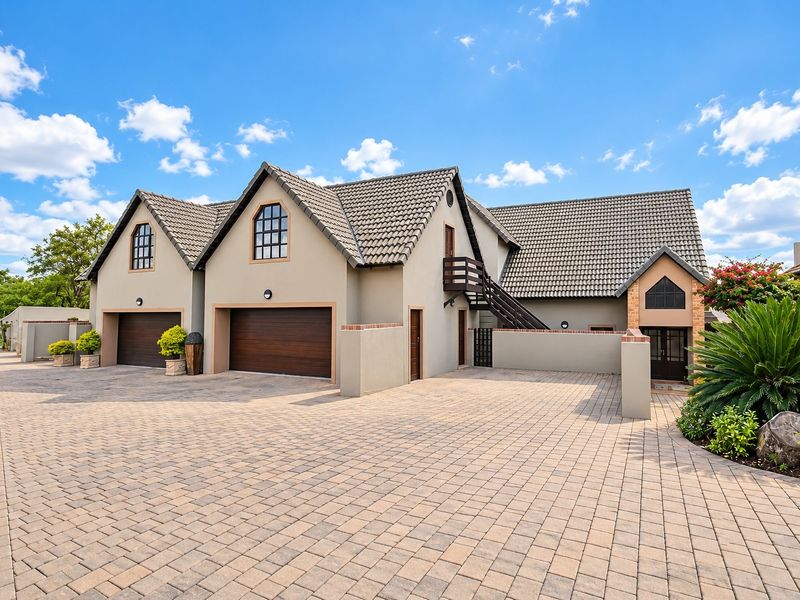 A well-maintained front exterior view featuring a double garage, paved driveway, and distinctive architectural roof lines with an external staircase.
