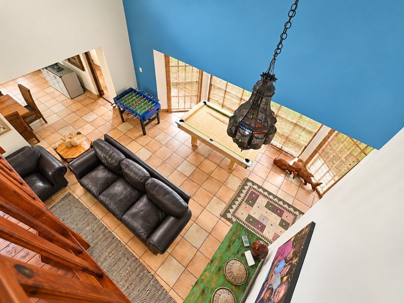Spacious double-volume living area featuring tiled flooring, a decorative pendant light, and a wooden staircase, offering an open and airy atmosphere.