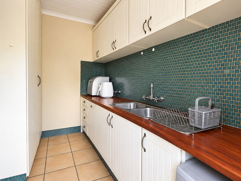 A functional scullery featuring white cabinetry, a warm timber countertop, a double stainless steel sink, and a decorative green mosaic tile backsplash.