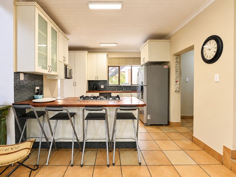 A functional kitchen featuring cream cabinetry, a timber breakfast bar with integrated gas hob, mosaic splashbacks, and durable ceramic floor tiles.