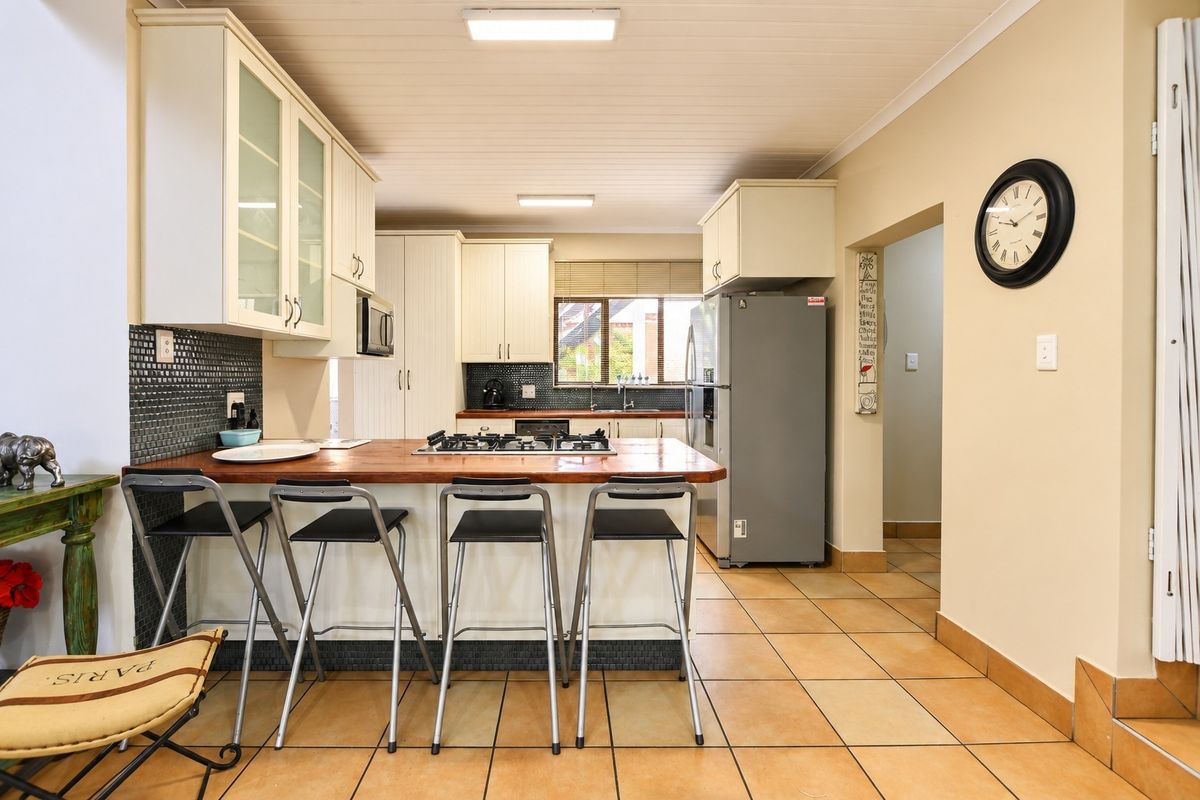 A functional kitchen featuring cream cabinetry, a timber breakfast bar with integrated gas hob, mosaic splashbacks, and durable ceramic floor tiles.
