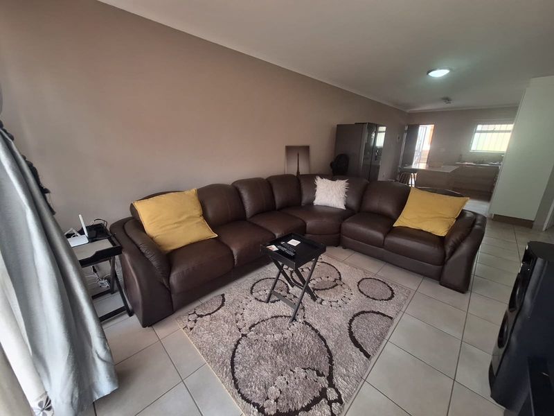 Open-plan living area featuring neutral wall tones and tiled flooring, seamlessly connecting to the kitchen space in the background.