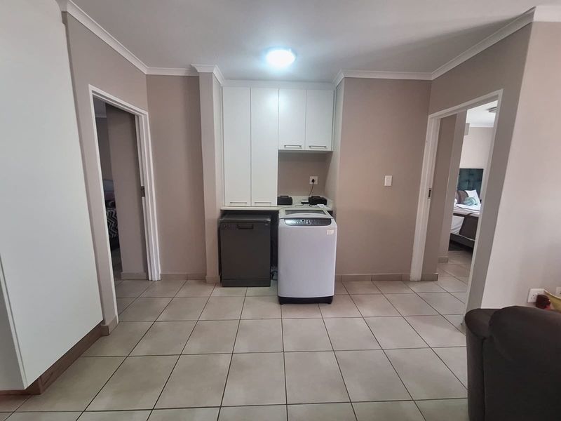A functional laundry area featuring built-in white cabinetry and tiled flooring, conveniently situated between two doorways.