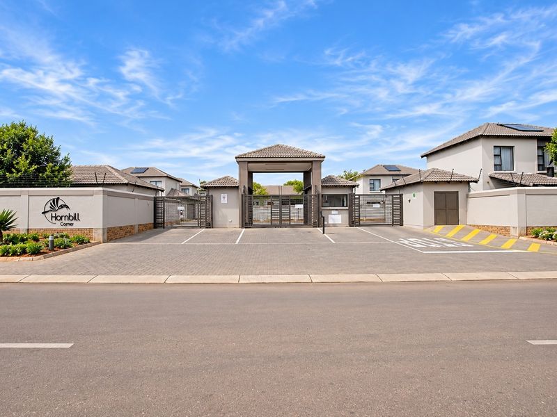 The secure entrance to Hornbill Corner townhouse complex, featuring a paved driveway, perimeter walling with electric fencing, and a gated access point.