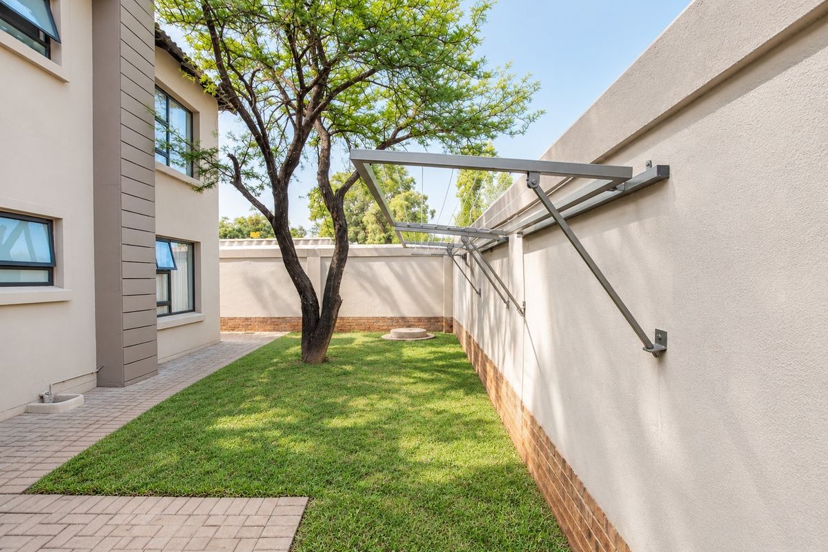 A well-maintained rear garden area featuring brick paving, a manicured lawn, and a practical wall-mounted clothesline against the boundary wall.