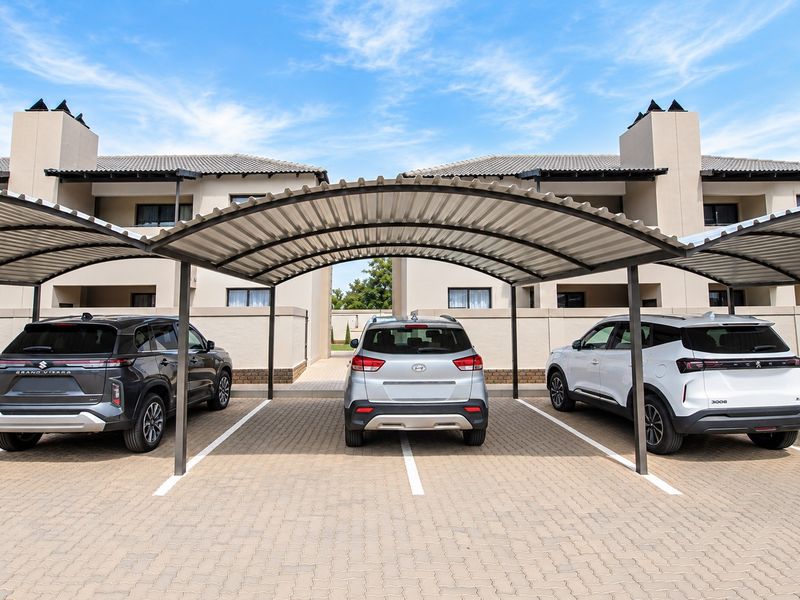 Covered carport parking area with paved driveway and modern townhouse facade in the background.
