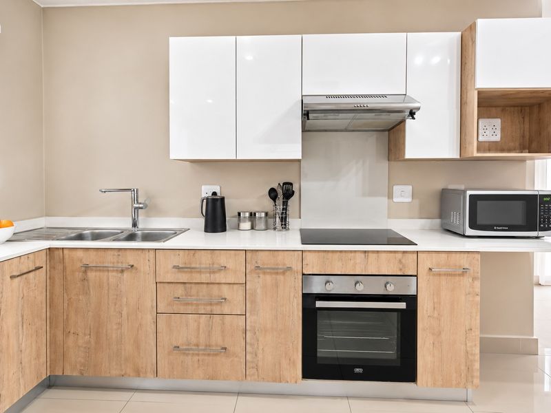 Modern kitchen featuring light wood-grain cabinetry, white high-gloss upper cabinets, stone countertops, integrated electric hob, oven, and extractor fan.