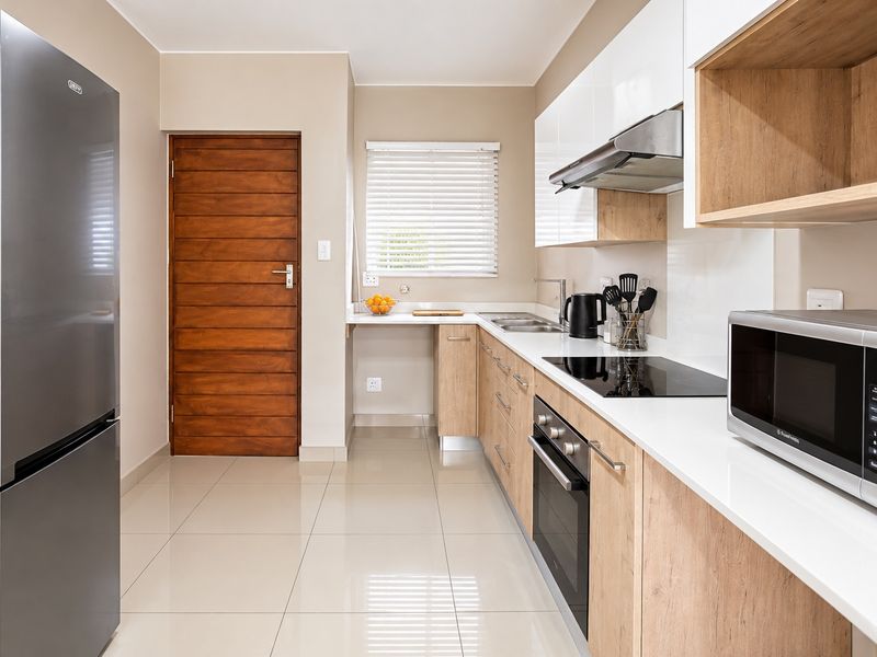 Modern galley-style kitchen featuring sleek white and wood-grain cabinetry, stone countertops, integrated appliances, and polished tiled flooring.