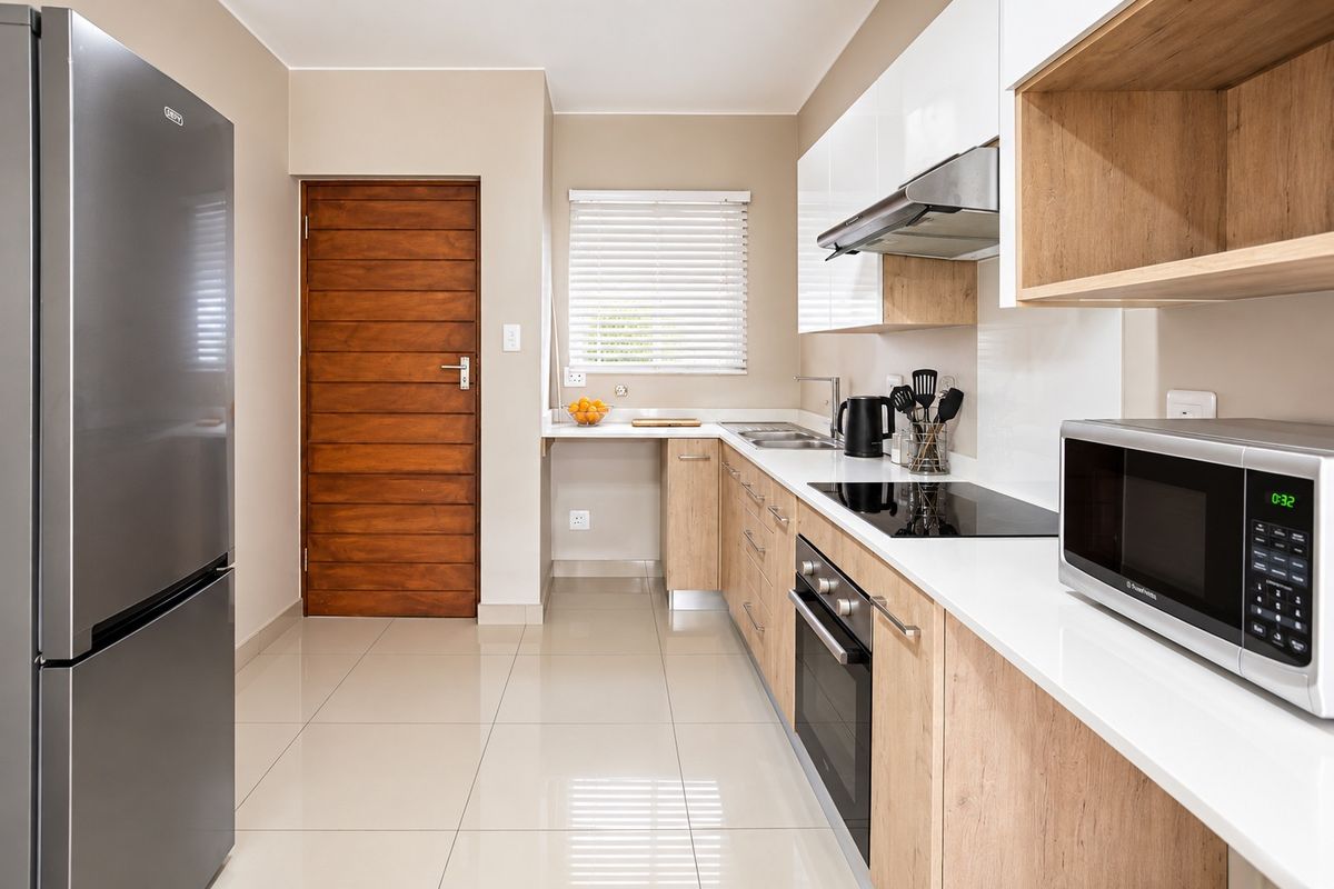 Modern galley-style kitchen featuring sleek white and wood-grain cabinetry, stone countertops, integrated appliances, and polished tiled flooring.