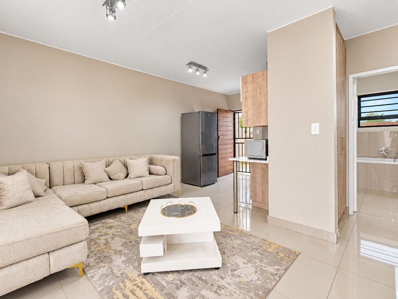 An open-plan living area featuring neutral tiled flooring, modern spotlight lighting, and integrated cabinetry, with a view into the adjacent bathroom.