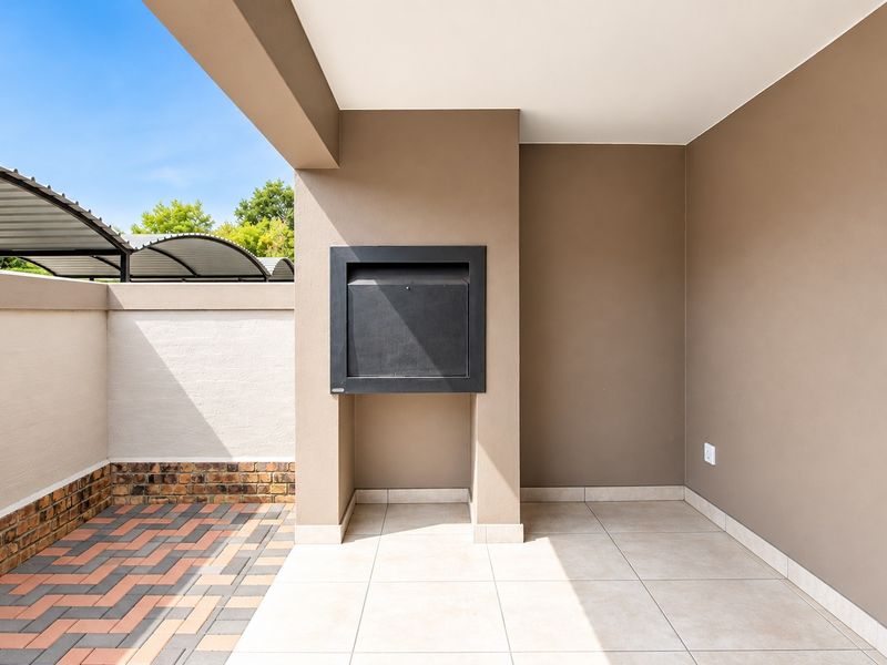 Covered patio area featuring a built-in braai, tiled flooring, and a private paved courtyard, ideal for outdoor entertaining.