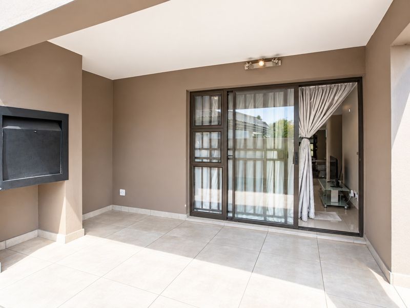 A clean, covered patio featuring tiled flooring, a built-in braai, and sliding glass doors providing access to the interior living space.