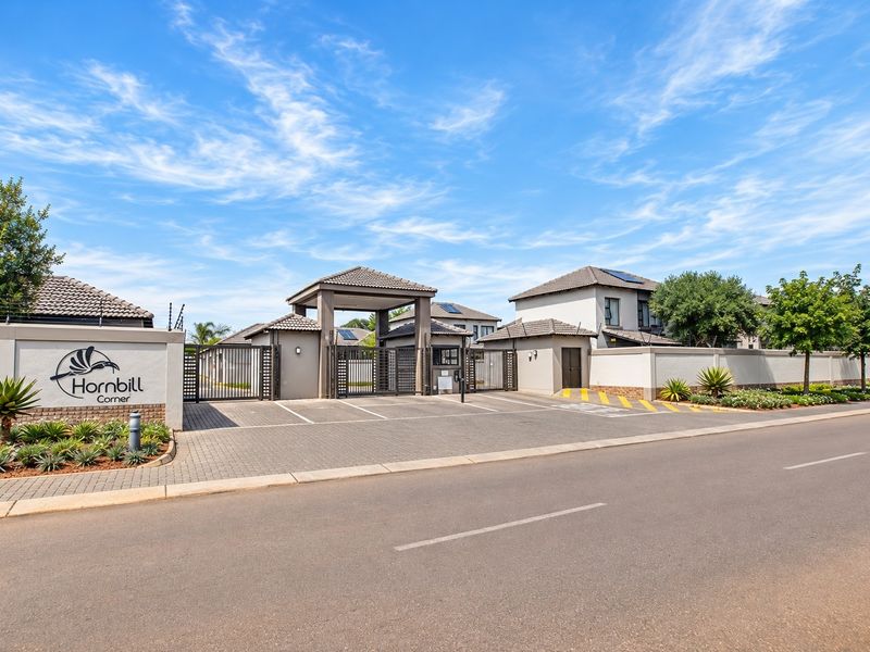 Front entrance view of Hornbill Corner townhouse complex, featuring a secure gated access point, paved driveway, and well-maintained perimeter walling.