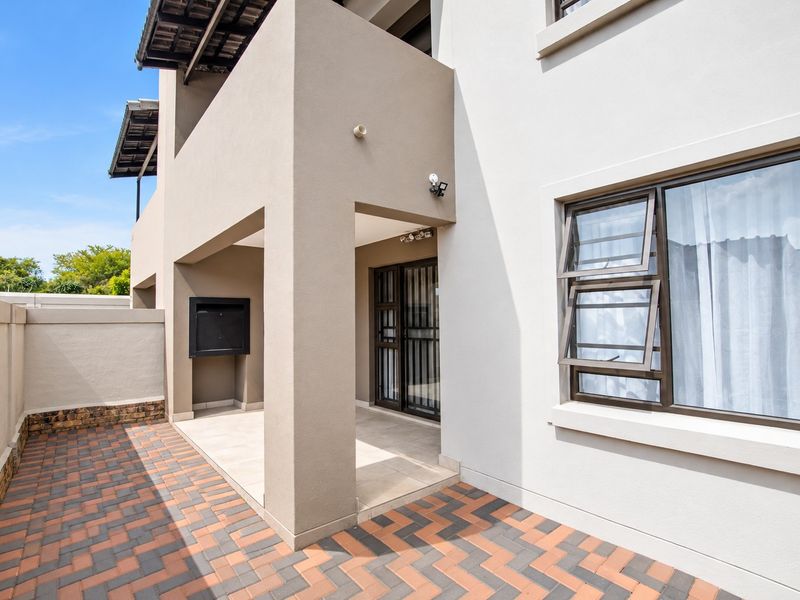 A well-maintained covered patio area featuring paved flooring and a built-in braai, providing a functional outdoor entertainment space.