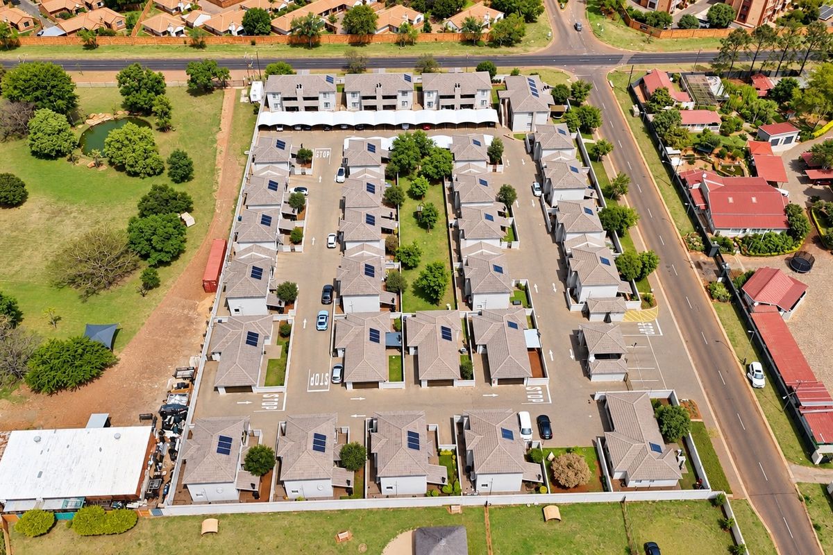 Aerial view of a townhouse complex featuring multiple residential units, paved internal roads, carports, and solar panel installations on the roofs.