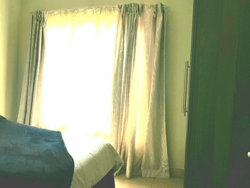 A bedroom featuring tiled flooring and a built-in wardrobe, with natural light entering through a window dressed with curtains.