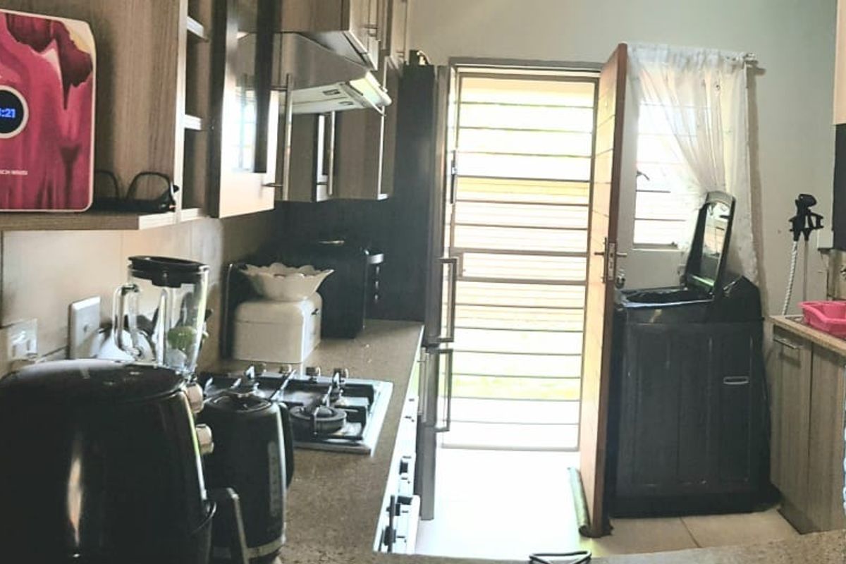 A functional kitchen featuring built-in cabinetry, stone countertops, a gas hob with extractor fan, and direct access to an exterior area via a security gate.